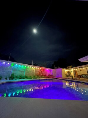 A nighttime pool area with a moonlit sky, illuminated walls, and a clear pool reflecting lights. - Tamarindo Sunset Beach House, Costa Rica Pura Vida! (Tamarindo)