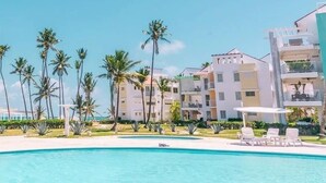 A resort with a swimming pool, palm trees, and multi-story buildings with balconies. - Playa Turquesa Ocean Club, A-203, cozy 1-BR apartment, AC, WiFi, private beach (Bavaro)