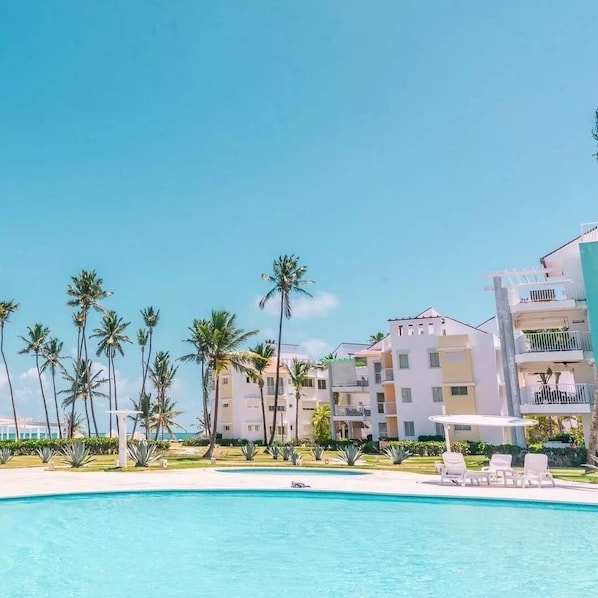 Un complexe hôtelier doté d’une piscine, de palmiers et d’immeubles à plusieurs étages avec des balcons.