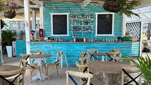 A bar area with wooden tables and chairs, a turquoise bar counter, and hanging plants. - Playa Turquesa Ocean Club, A-203, cozy 1-BR apartment, AC, WiFi, private beach (Bavaro)