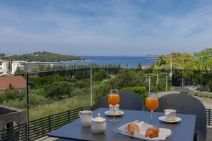 Une table dressée avec des aliments pour le petit-déjeuner, offrant une vue panoramique sur la mer et les collines.