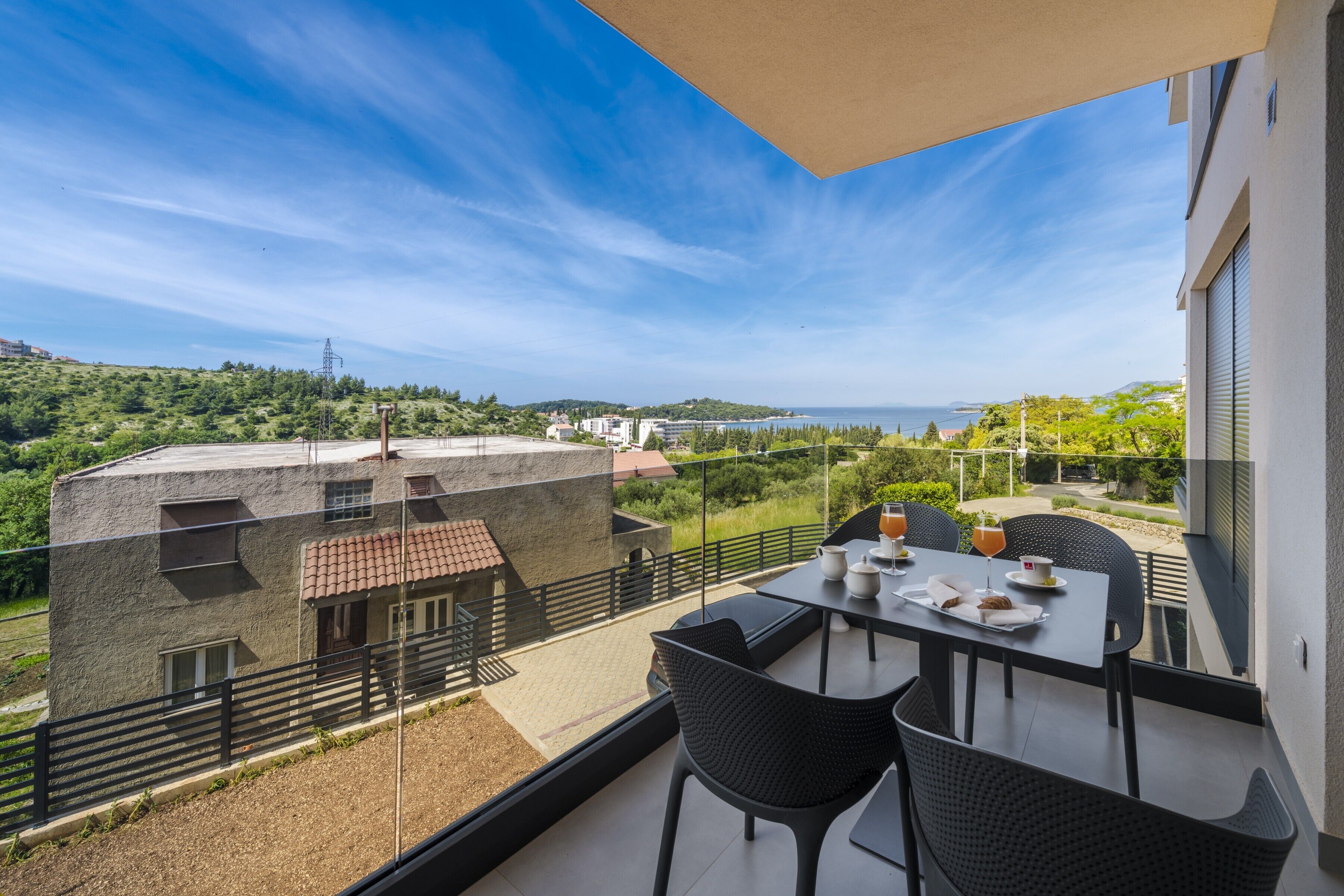 Ein Balkon mit Tisch, Stühlen und Blick auf das Meer und die grüne Umgebung.