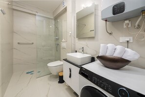Une salle de bain moderne avec une douche à parois de verre, un lavabo blanc et un lave-linge encastré.