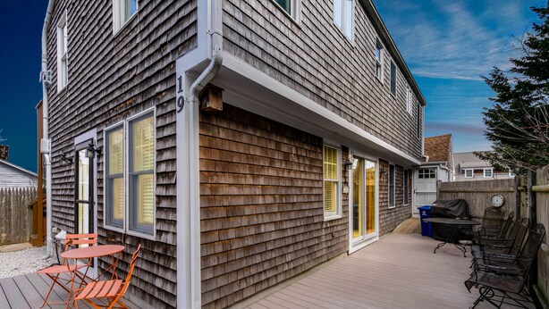 A wooden deck with outdoor furniture, a covered patio area, and a view of neighboring houses.