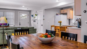 A modern kitchen with wooden cabinets, a dining table with chairs, and a bowl of fruit.
