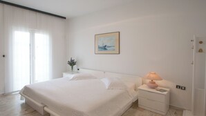 Un dormitorio con una cama grande, una mesita de noche, una lámpara, un cuadro en la pared y una ventana con cortinas.