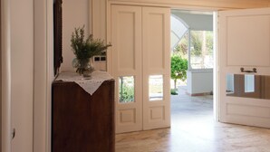 Un pasillo con un banco de madera, un jarrón con plantas y una puerta que da a un espacio exterior luminoso.