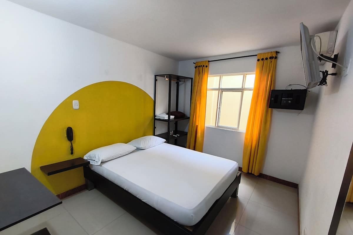 Een hotelkamer met een bed, een bureau, een telefoon, een raam met gordijnen en een wandairconditioner.