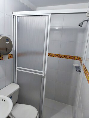 A bathroom with a toilet, a sink, a shower with a glass door, and a tiled shower area. - Hotel Cielo de Tambores (Cali)