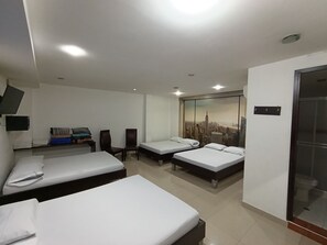 A hotel room with two single beds, a desk with a chair, a TV mounted on the wall, and a large window with a cityscape view. - Hotel Cielo de Tambores (Cali)