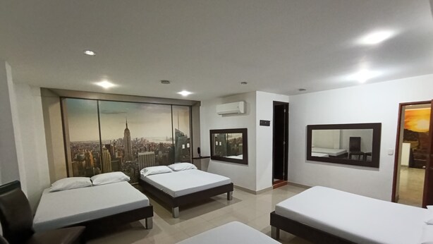 A hotel room with three beds, a large window with a cityscape view, a mirror, and an air conditioning unit. - Hotel Cielo de Tambores (Cali)