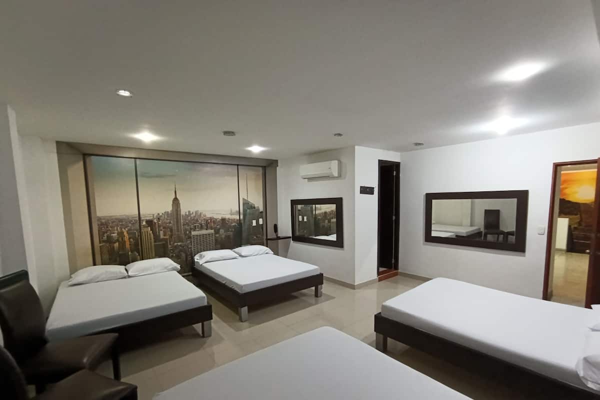 Hotelkamer met drie bedden, een groot raam met uitzicht op de stad, een spiegel en een airconditioning.