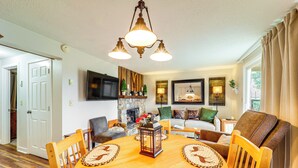 A dining area with a wooden table, chairs, and a chandelier. There is a fireplace and a television mounted on the wall.