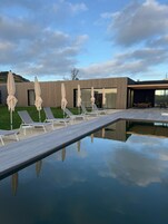 Una piscina al aire libre, sombrillas, sillones reclinables de piscina