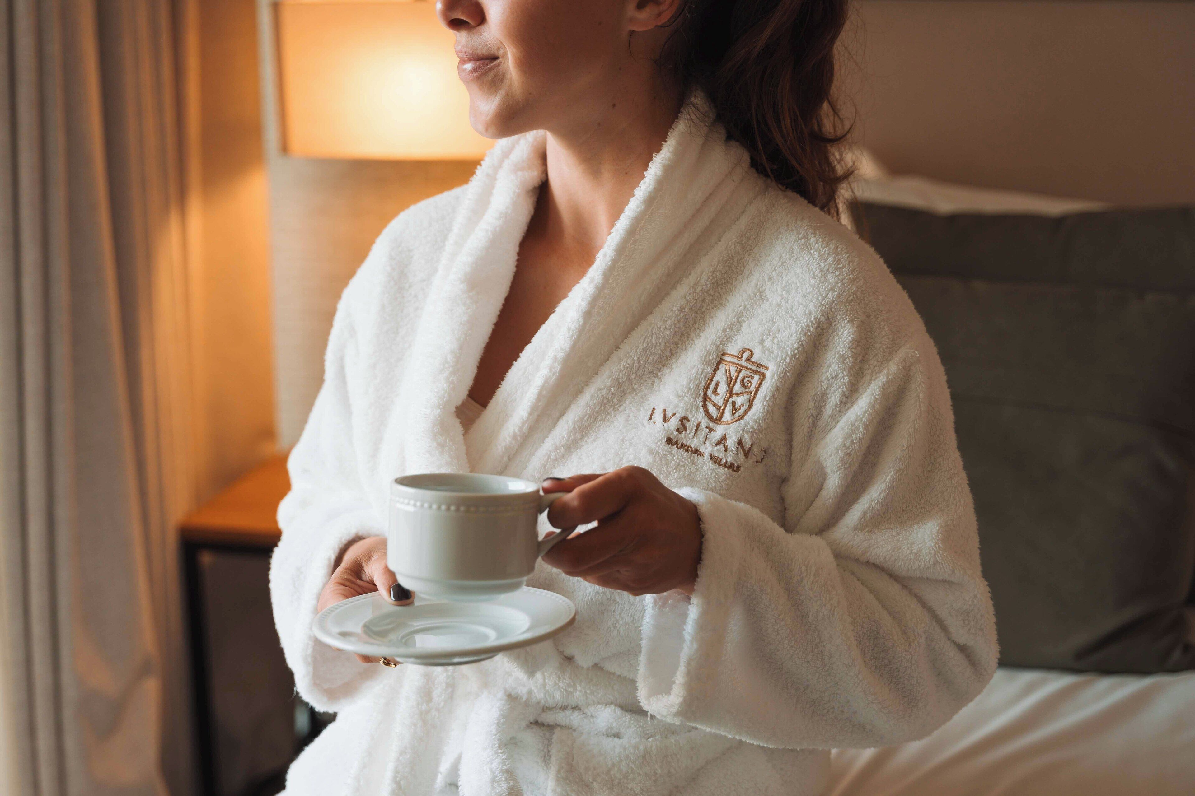 Une personne vêtue d’une robe blanche, tenant une tasse et une soucoupe, la robe étant ornée d’un logo.
