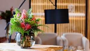 Una mesa de madera con un florero de vidrio, un interior moderno con un sofá y una televisión de pantalla plana al fondo.