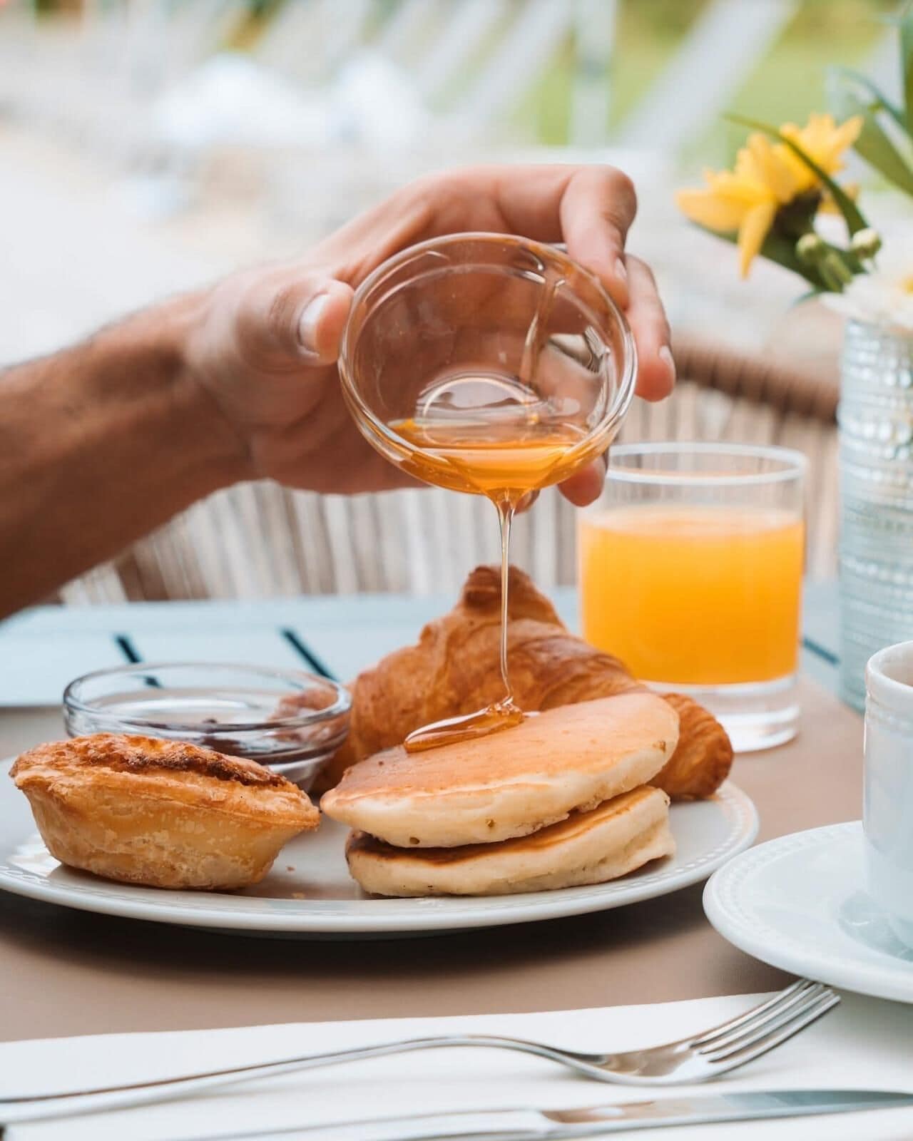 Un desayuno con tortitas, un croissant y un vaso de zumo de naranja sobre una mesa.
