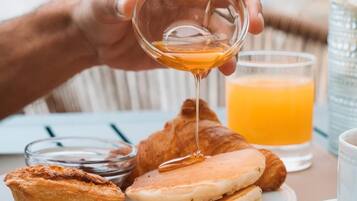 Un desayuno con tortitas, un croissant y un vaso de zumo de naranja sobre una mesa.