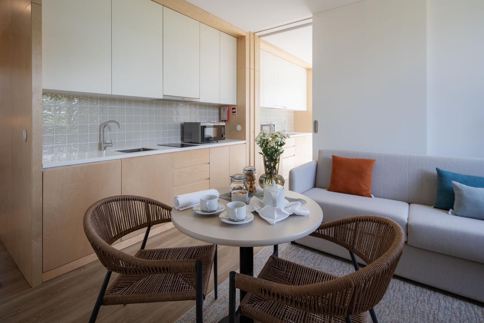 A modern kitchen with white cabinets, a microwave, and a dining area with wicker chairs and a round table.