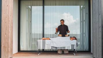 Een moderne massagesruimte buiten, met een massagetafel, een masseur en een cliënt die op haar buik ligt.