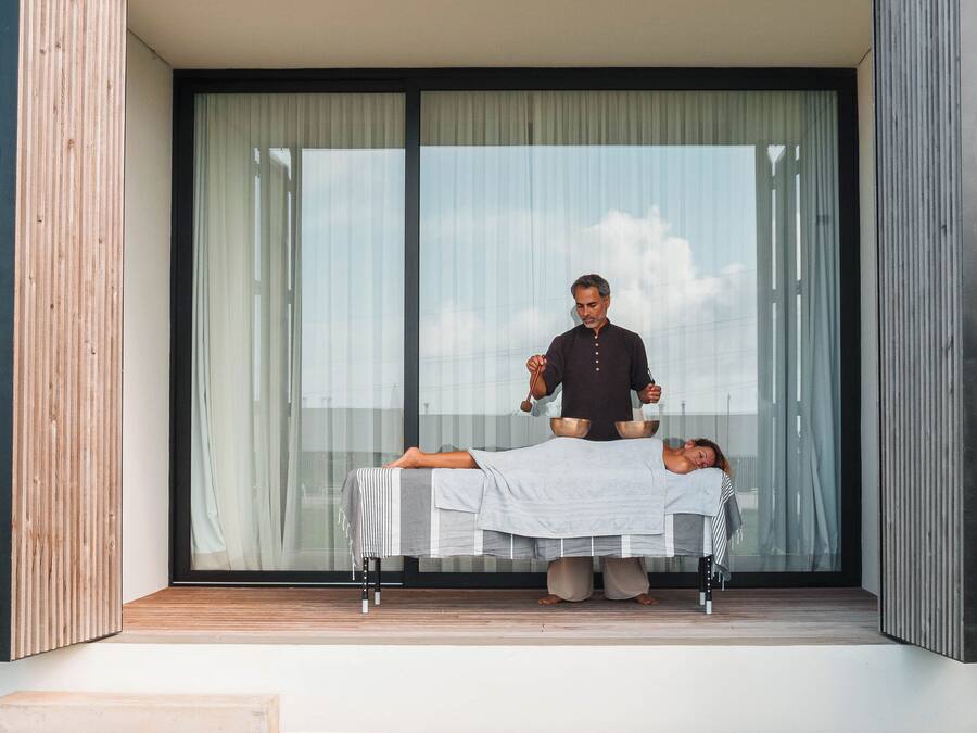 Een moderne massagesruimte buiten, met een massagetafel, een masseur en een cliënt die op haar buik ligt.