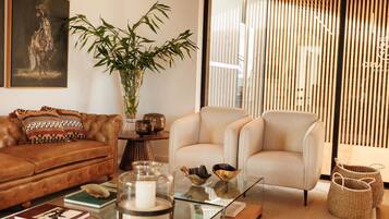 A modern living room with a leather sofa, a glass coffee table, and a beige armchair. A large bamboo plant is in the corner, and there are decorative bowls on the table.