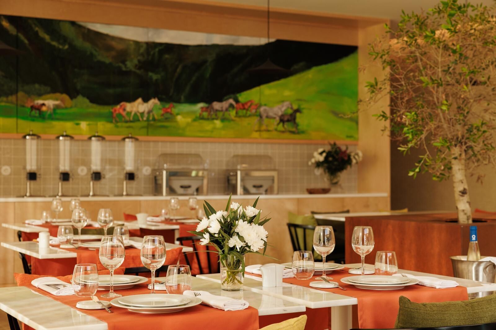 Un restaurante con mesas dispuestas para comer, un cuadro en la pared y una planta en maceta.