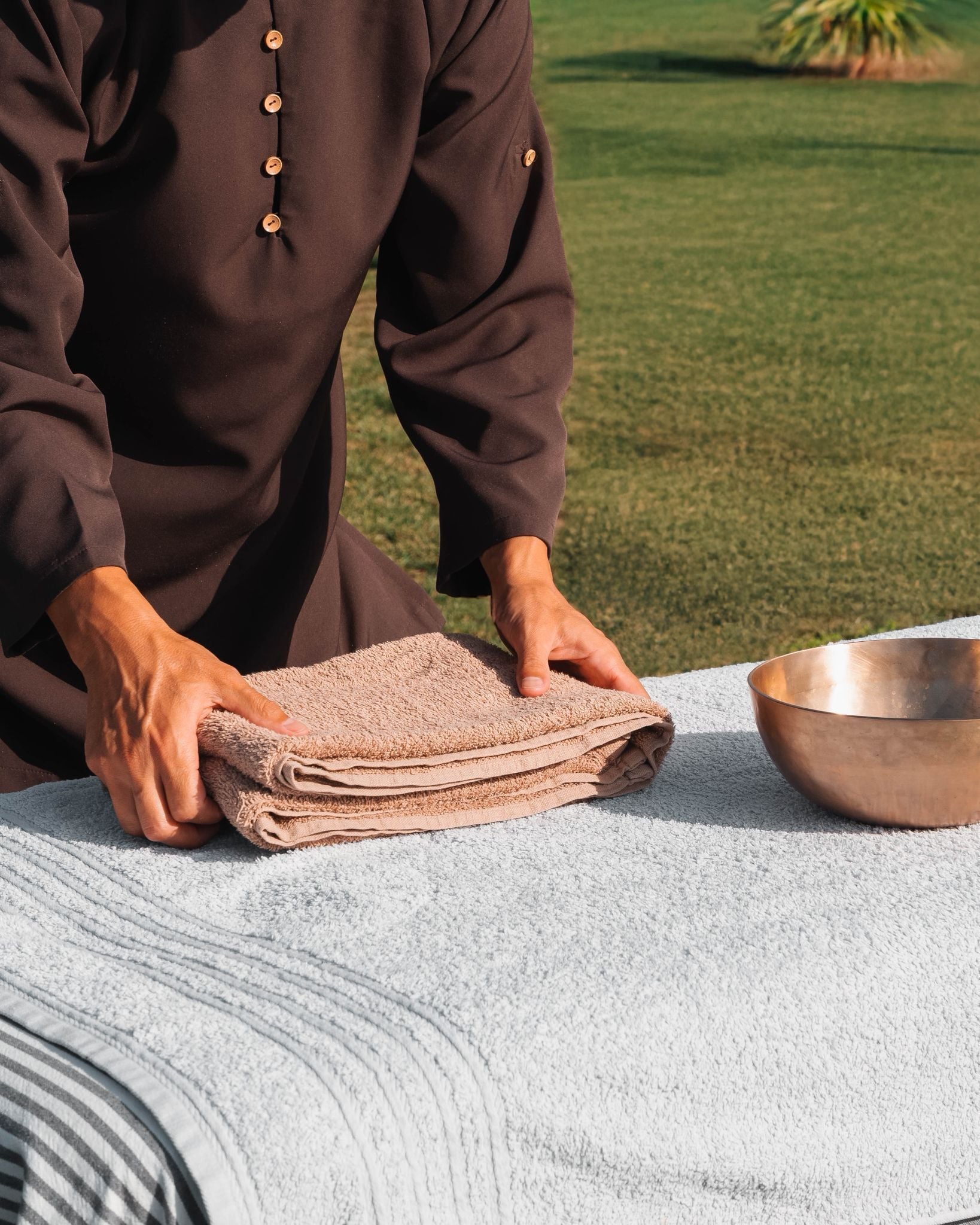 A person folding a towel on a table with a bowl beside it.