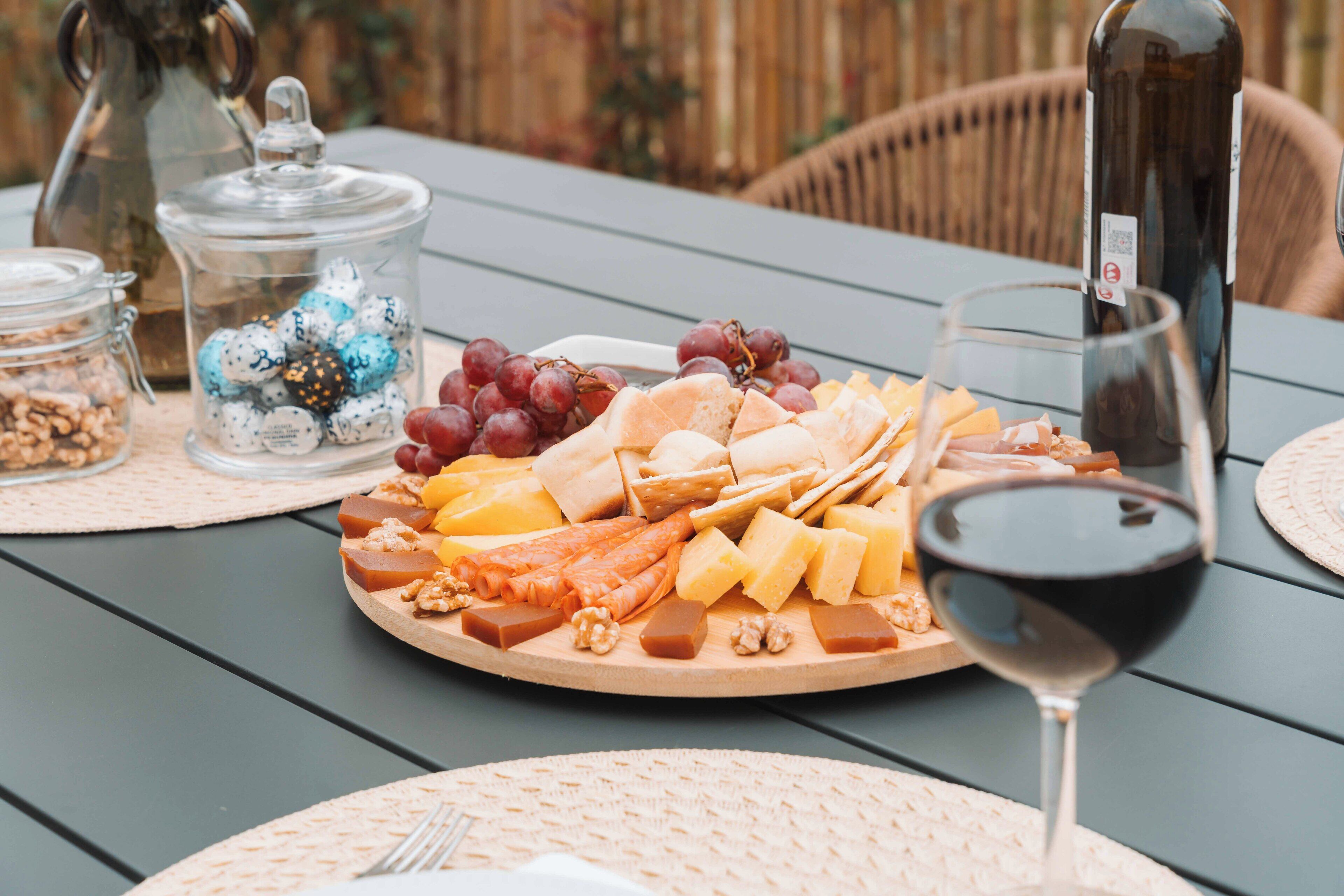 A table with a cheese platter, grapes, walnuts, and a wine glass.