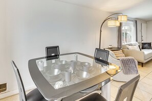 Un espace repas moderne avec une table à plateau en verre, plusieurs chaises et une table d’appoint avec une lampe.