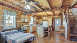 Un chalet rustique avec un intérieur en bois, un espace cuisine central, une table à manger et un escalier.
