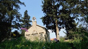 A stone building with a bell tower, surrounded by trees and greenery.