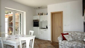 A compact kitchen with white cabinets, a dining table with chairs, and a sofa with a red pillow.