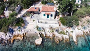 A coastal house with a tiled roof, a small garden, and a rocky shoreline.