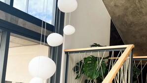 Een moderne trap met een houten leuning en touwdetails, die leidt naar een plateau met hangende bolvormige lampen en een potplant.