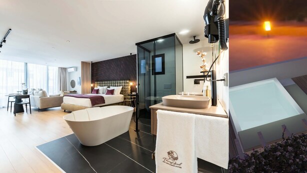 Een modern hotelinterieur met een groot bad, een douche met glazen wanden en een gezellige zithoek met een bank en stoelen.