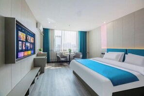Quarto de hotel moderno com uma cama grande, televisão de tela plana na parede, uma mesinha com cadeiras e vista para a cidade através de amplas janelas.