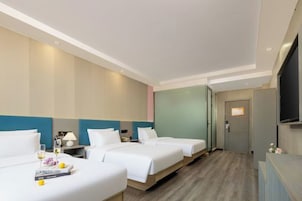 A hotel room with three beds, a television, and a door leading to a bathroom.