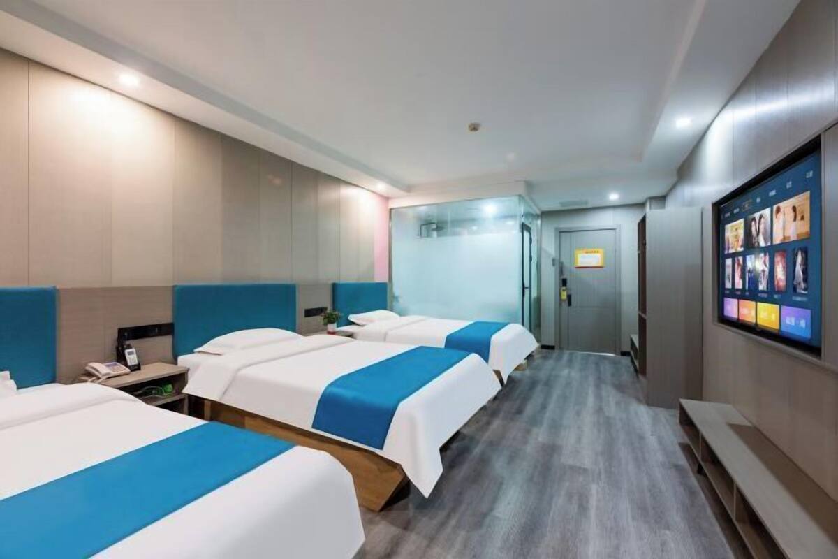 A hotel room with three beds, a TV screen, and a hallway leading to a door.