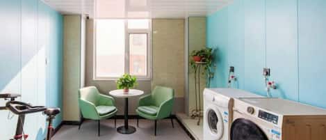 A laundry room with a washing machine, two chairs, a table with a plant, and a bicycle.