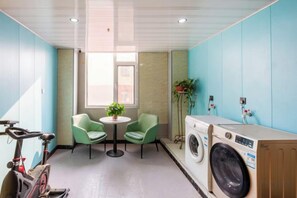 A laundry room with a washing machine, two chairs, a table with a plant, and a bicycle. - Lanting Hotel (Liaocheng Wanda Plaza Branch) (Liaocheng)