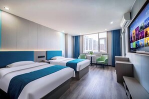 Quarto de hotel com duas camas, televisão, uma mesinha e janela com vista para edifícios.