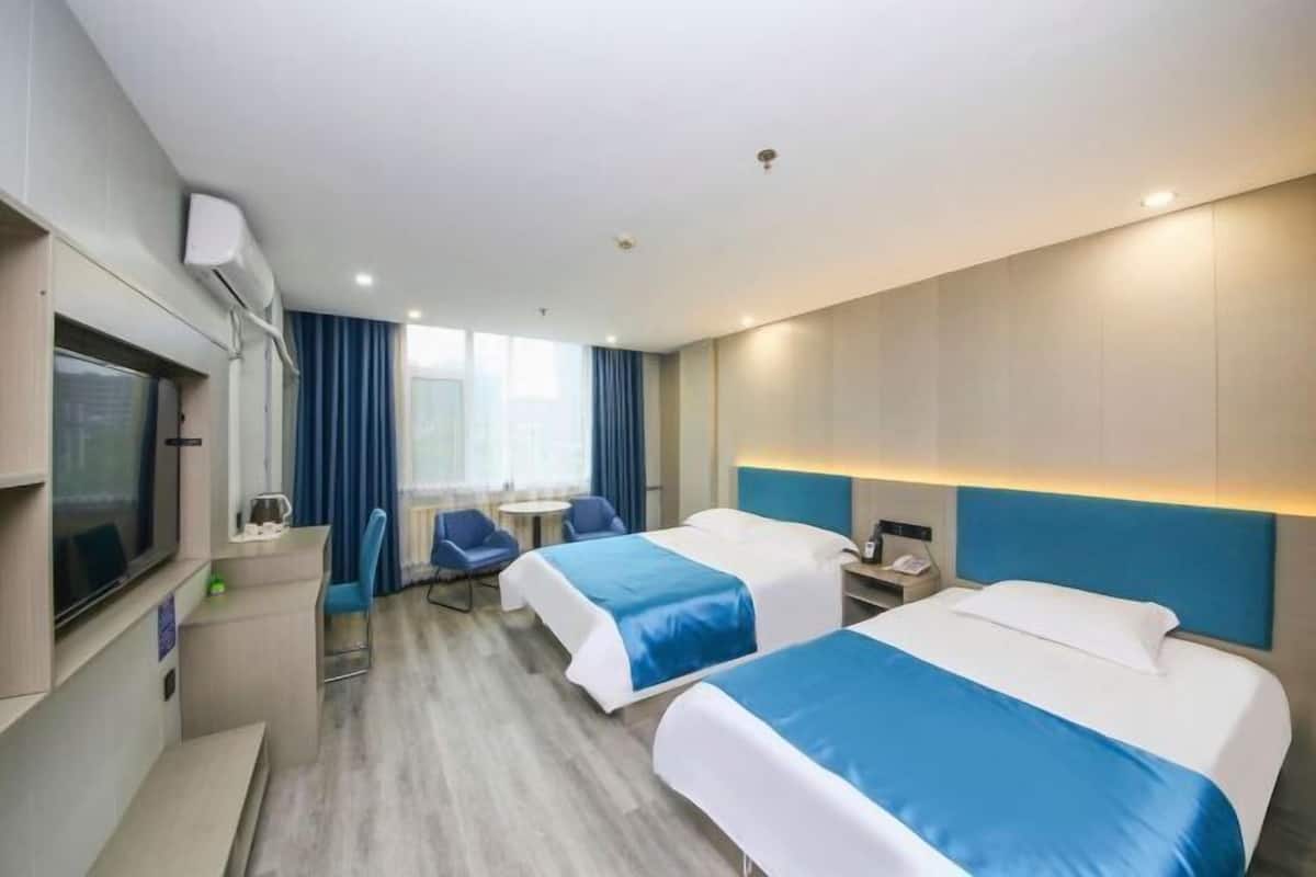 A hotel room with two beds, a desk, a chair, a TV, and a window with curtains.