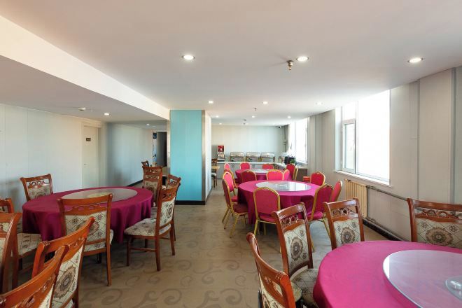Un comedor con mesas y sillas redondas, una cocina al fondo y vistas al exterior a través de amplios ventanales.