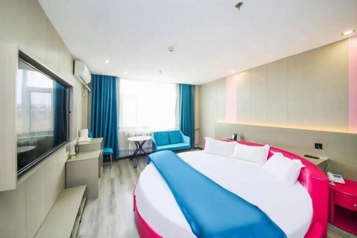 A hotel room with a large bed, a desk, a chair, a small table, and a window with curtains.