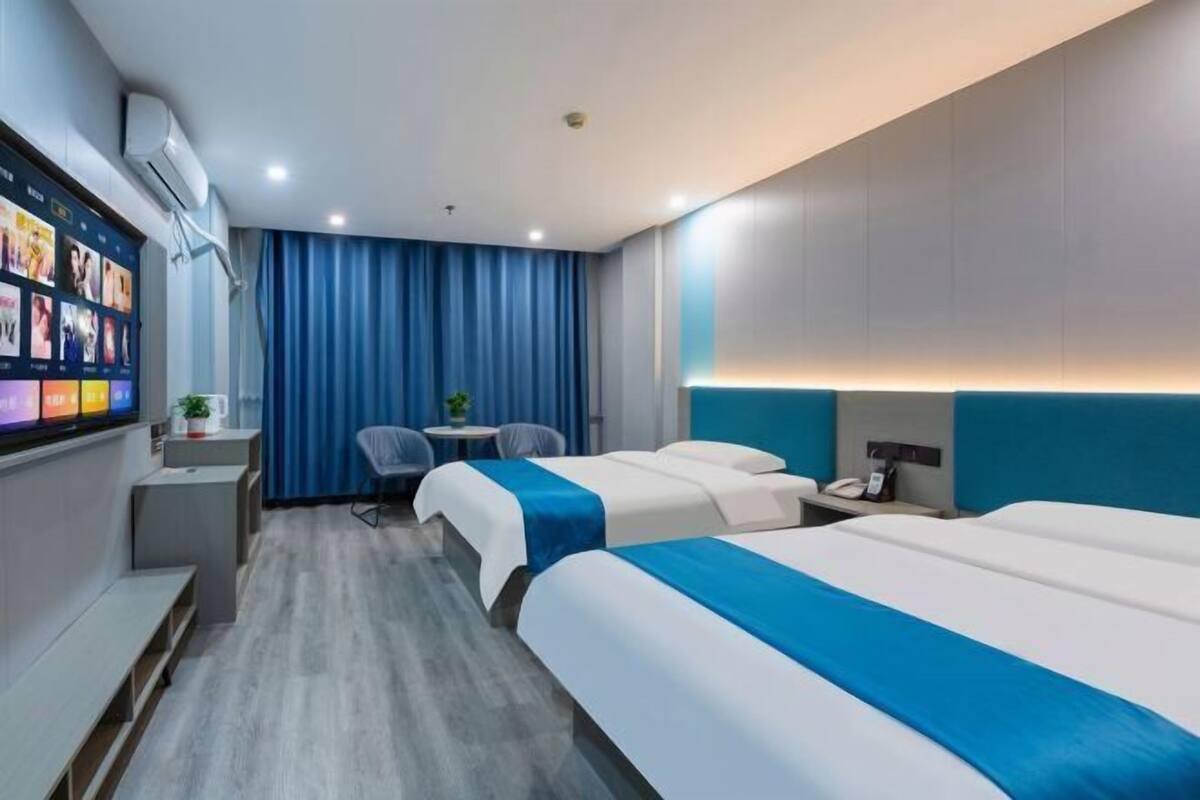 A hotel room with two beds, a desk, a chair, a small table, and a TV screen displaying images.