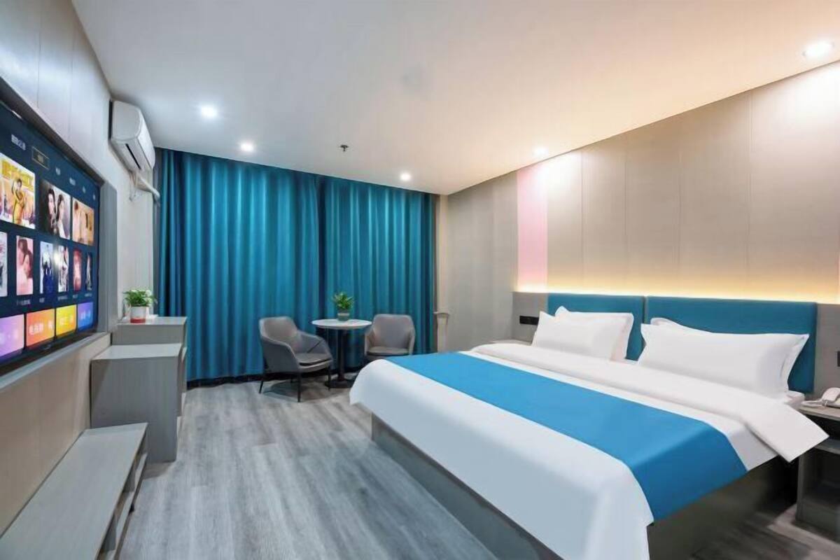 A hotel room with a large bed, a desk with a chair, a small table with two chairs, and a wall-mounted TV.
