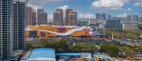 A high-rise building with a curved facade, surrounded by other high-rise buildings, a parking lot with various vehicles, and a construction crane in the background.