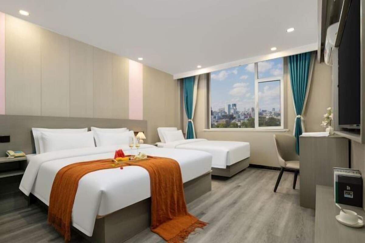 A hotel room with two beds, a desk, a chair, a TV, and a window with a city view.