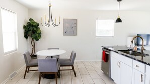 Une cuisine moderne avec des armoires blanches, un comptoir noir et un évier en acier inoxydable. On y trouve une table à manger avec quatre chaises et un lustre au-dessus.